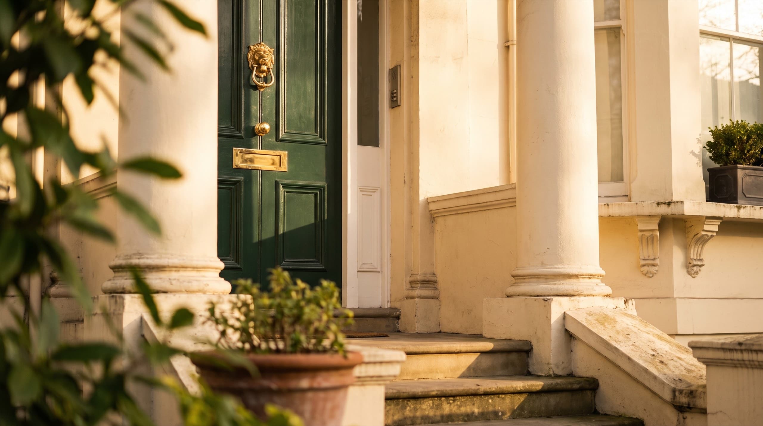 Deep green London period front door with polished brass in warm evening light